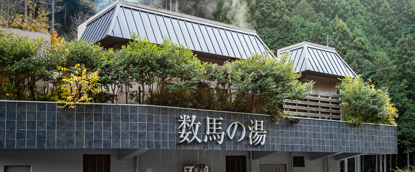 「数馬の湯」の看板。建物の奥から湯気が立ち上っている