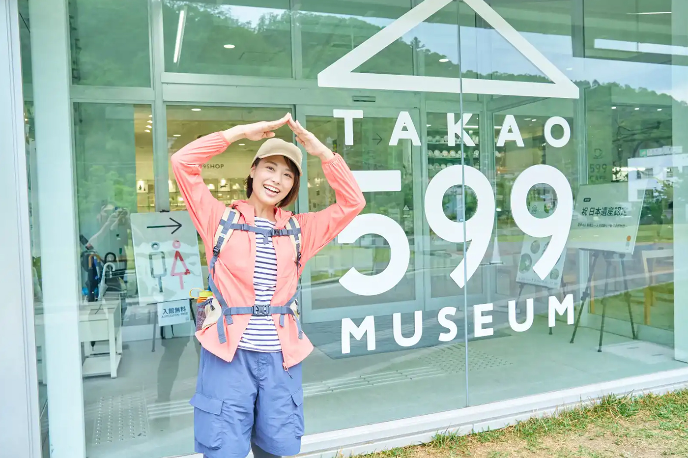 山をモチーフにしたロゴが描かれたガラス張りのおしゃれな外観の前で山のポーズをきめるかほさん