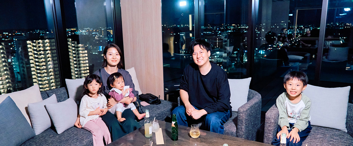 ソラノホテルからの夜景を背に、ソファに座ってドリンクを楽しむおりおりん一家